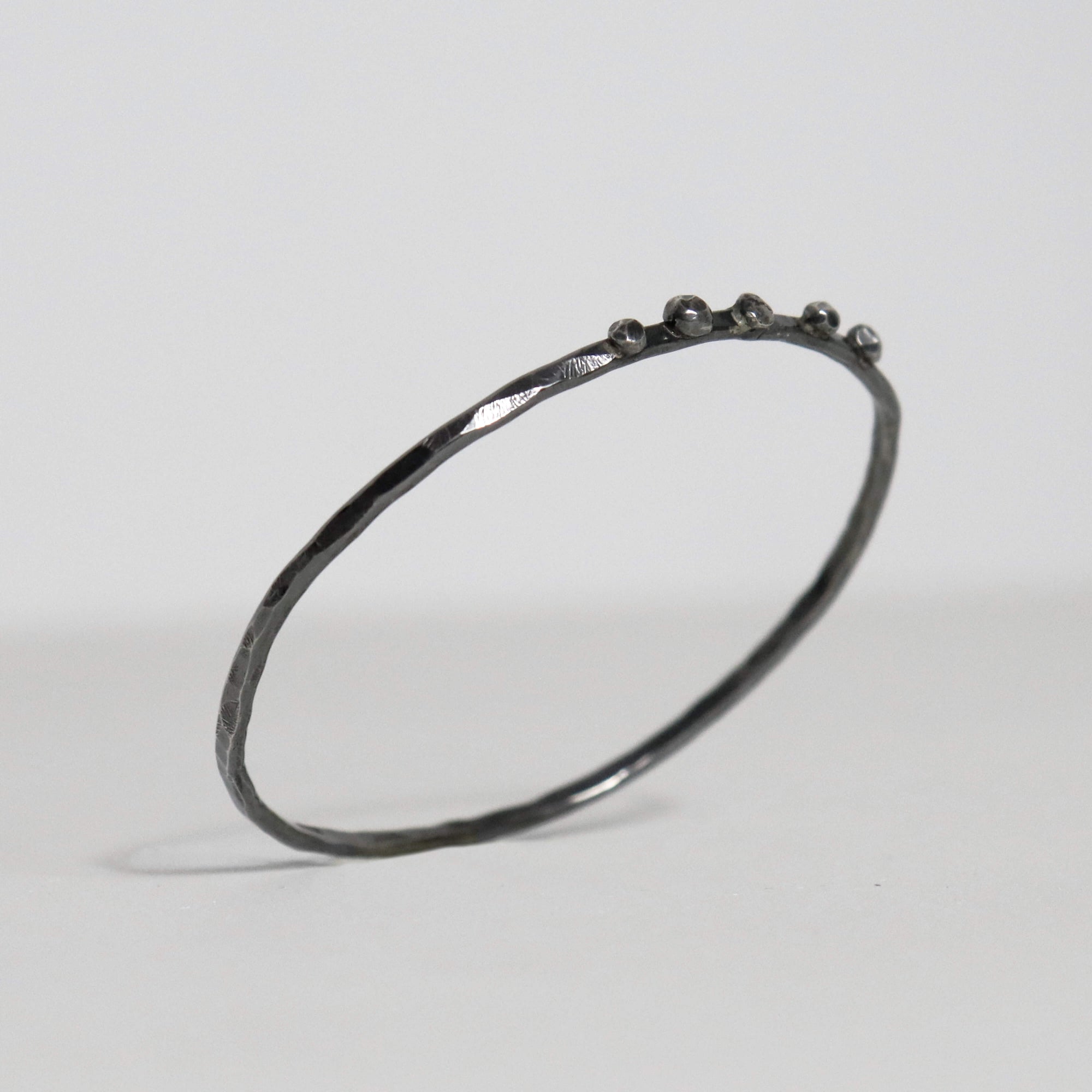 Handmade oxidized sterling silver bangle with hammered texture and five fused silver nuggets along the upper edge.