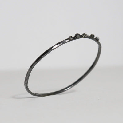 Handmade oxidized sterling silver bangle with hammered texture and five fused silver nuggets along the upper edge.