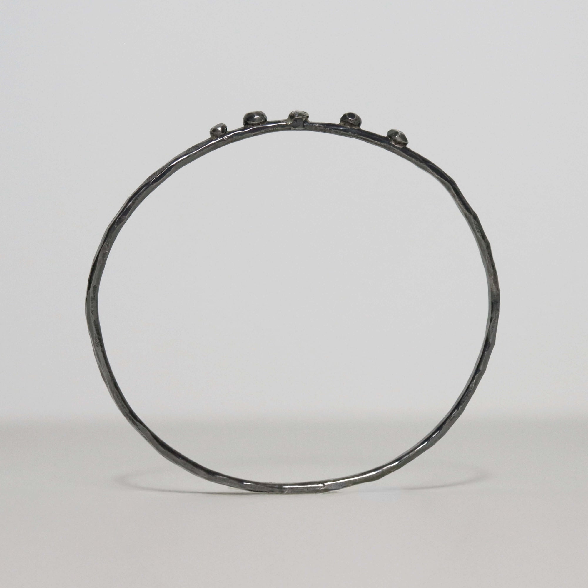 Slender handmade sterling silver bangle with dark oxidized finish, faceted hammered band and five small silver nuggets.