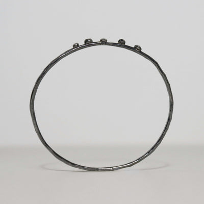 Slender handmade sterling silver bangle with dark oxidized finish, faceted hammered band and five small silver nuggets.