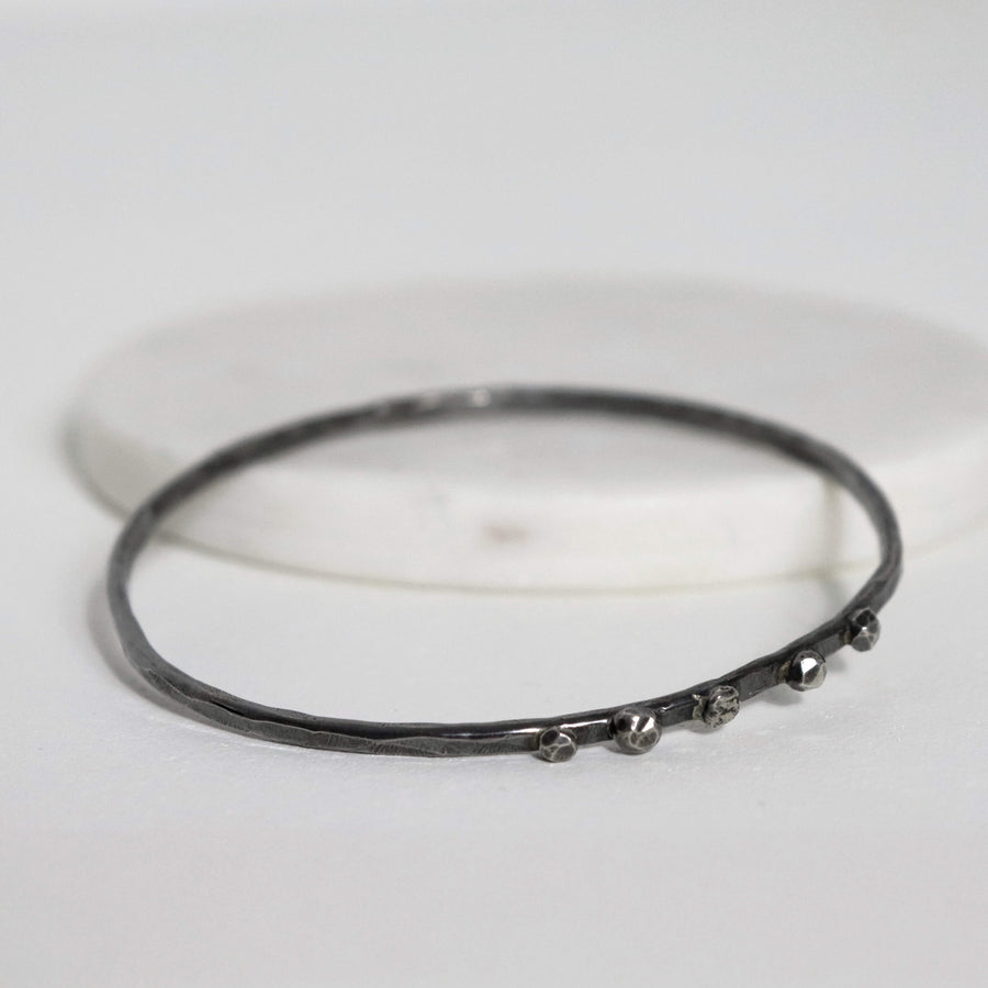 Textured sterling silver nugget bangle lying flat, showing its irregular hammered surface and raised fused silver details.