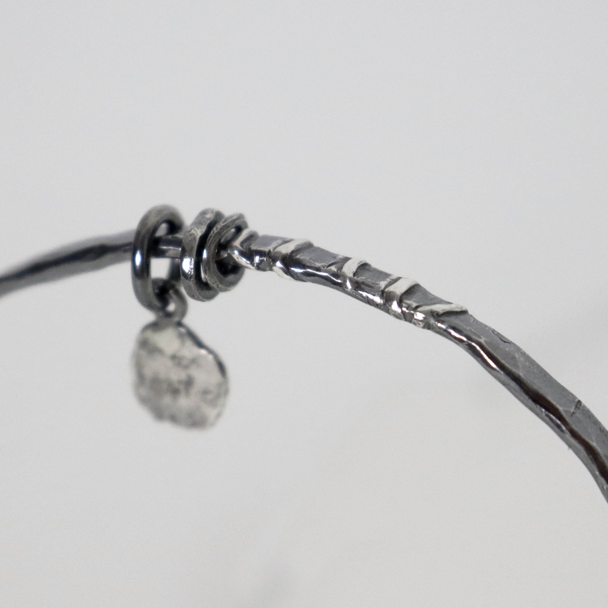 Close-up of Raw silver bangle by Roff Jewellery showing soldered silver lines, dark oxidized texture and loose silver rings
