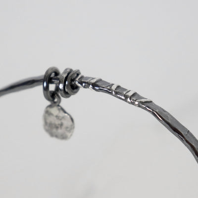 Close-up of Raw silver bangle by Roff Jewellery showing soldered silver lines, dark oxidized texture and loose silver rings
