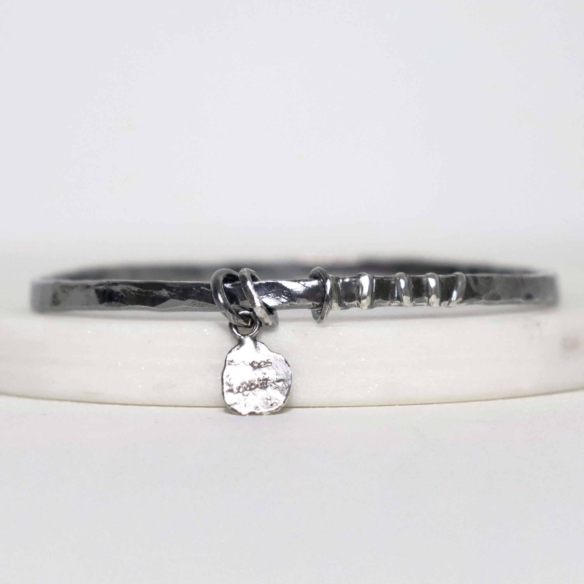 Textured sterling silver bangle by Roff Jewellery with a small dangling Roff stamped charm and irregular polished silver detail
