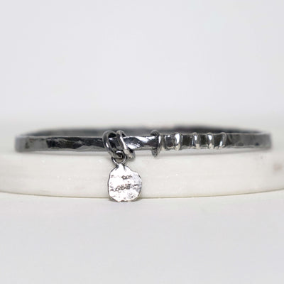 Textured sterling silver bangle by Roff Jewellery with a small dangling Roff stamped charm and irregular polished silver detail