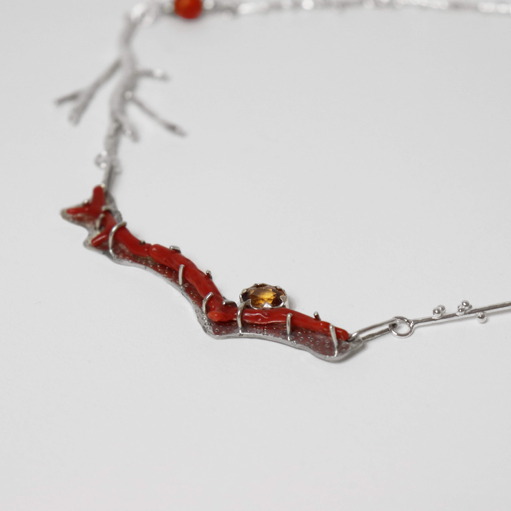 detail of silver necklace with coral-shaped pendant featuring red coral,carnelian beads and a central zircon gemstone handmade by roff