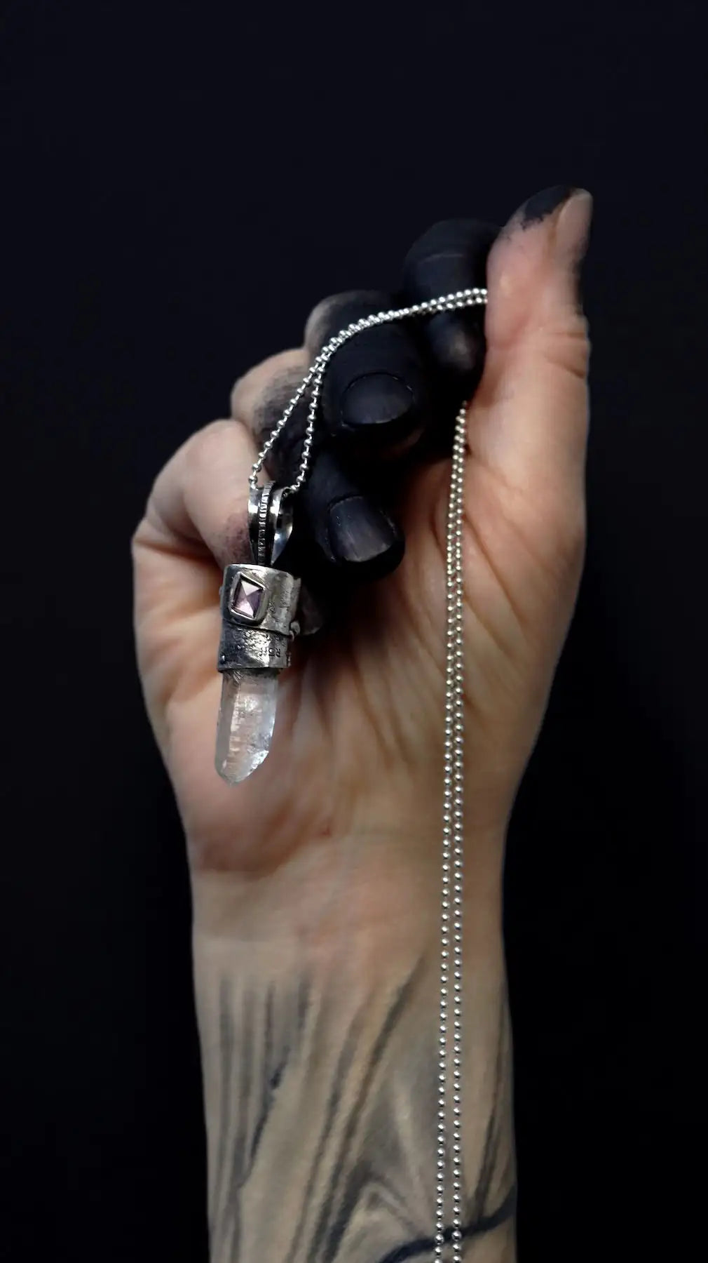 silver necklace set with crystal and beryl pendant held by hand of  which the fingers are covered in soot