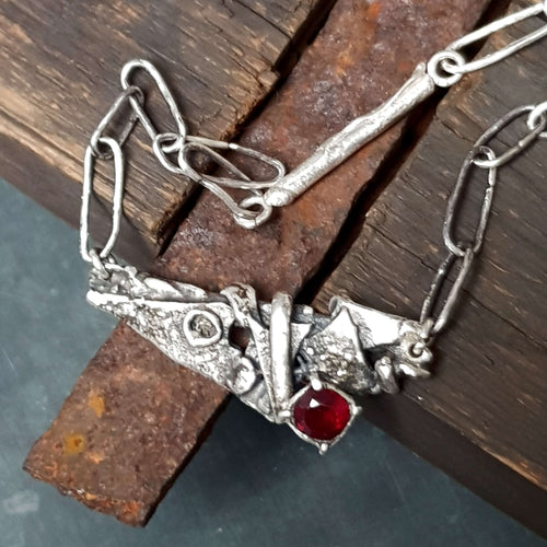 rustic necklace with handmade raw silver links, brutalist pendant in oxidized silver with rough texture and a red garnet gemstone