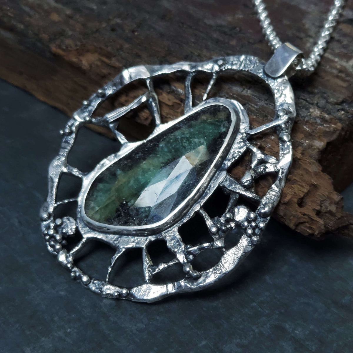 teardrop faceted emerald set in oxidized silver spiderweb wheel pendant, handmade by roff jewellery